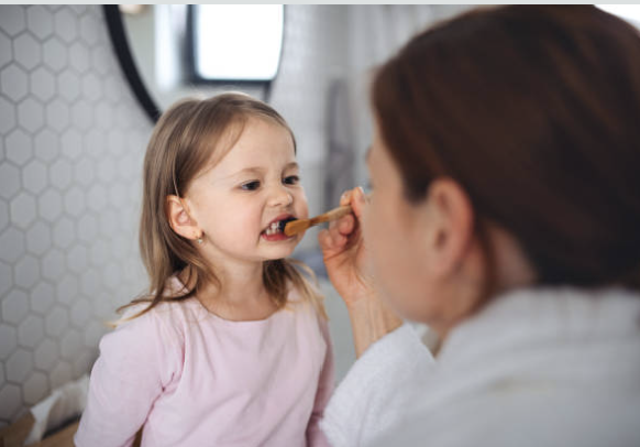 Mother helping her young child brush teeth at home to build healthy dental habits
